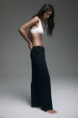 Pantalón de pijama confeccionado en punto pointelle suave, color negro con estampado de pequeños lunares blancos. Cuenta con perneras levemente acampanadas, cintura elástica con ribete de volados y cordón ajustable.