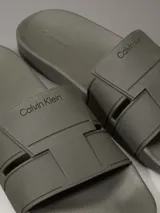 Ojotas tipo slide de color verde oliva, con doble tira superior de TPU con relieve y logotipo grabado. Cuentan con plantilla moldeada ergonómica con soporte para el arco plantar y suela de EVA.