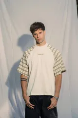 Remera unisex de jersey color blanco con mangas raglán a rayas horizontales en tonos verde oliva y blanco. Presenta un pequeño bordado en el pecho.