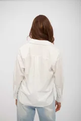 Camisa de corte clásico y silueta holgada, con cuello camisero, cierre frontal de botones y mangas largas con puños abotonados.