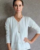 Remera blanca de manga larga con cuello en V y costuras decorativas en contraste. Incluye un lazo ajustable en el cuello con herraje metálico circular.