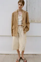 Top de color crema con escote en pico, tirantes anchos y cierre frontal de botones. Presenta bordados florales en tono verde claro alrededor del escote y en forma de semicírculo en la parte inferior delantera.