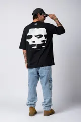 Remera blanca de corte oversize con cuello redondo y mangas cortas. Presenta un pequeño estampado tipográfico en la parte inferior frontal y un diseño gráfico de mayor tamaño en la espalda.