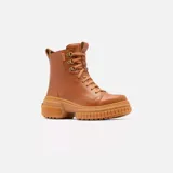 Bota de caña media Sorel, confeccionada en cuero impermeable color marrón tostado. Presenta un diseño moderno con cordones frontales, herrajes metálicos en forma de D y una suela de caucho robusta con plataforma dentada. Incluye tirador en el talón y cierre lateral para mayor practicidad.