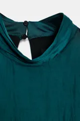 Vestido corto color verde azulado oscuro, con cuello alto y manga larga acampanada. Presenta volantes horizontales superpuestos en el cuerpo.
