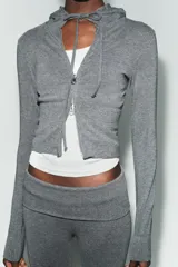 Sudadera cropped de punto con cierre frontal de cremallera metálica, capucha ajustable con cordones y mangas largas con puños en rib.