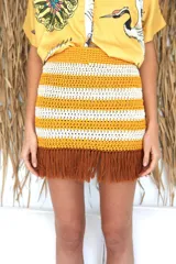 Minifalda tejida a mano en hilado de algodón, con diseño a rayas horizontales en color amarillo y blanco. Presenta flecos marrones en el ruedo.