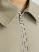 Campera estilo worker de corte recto, confeccionada en tejido plano Oxford de algodón color verde grisáceo. Presenta cuello clásico, cierre frontal completo con cremallera metálica, mangas largas con puños abotonados y bolsillos laterales integrados.