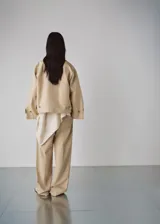 Chaqueta corta de algodón color beige, de corte holgado, con cuello clásico, cierre frontal de botones y bolsillos ribeteados. Cuenta con mangas largas amplias con puños ajustables mediante tiras y botones.