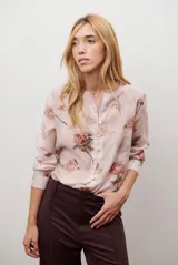 Camisa de manga larga con estampado floral en tonos rosados y cuello redondo con pequeña abertura frontal. Presenta cierre frontal con botones y puños abotonados.