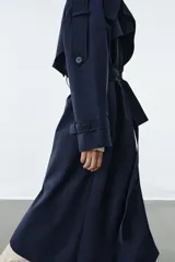 Trench oversize de Zara Woman Collection, color azul marino, confeccionado en hilatura con mezcla de algodón. Presenta cuello solapa, manga larga ajustable con trabillas, bolsillos delanteros y cinturón del mismo tejido con lazadas. Destacan los pespuntes marcados a tono y el cierre frontal cruzado con botones.