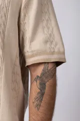 Camisa de punto de manga corta con cuello tipo bowling y cierre frontal de botones. Presenta un diseño texturizado con franjas verticales y detalles de contraste en blanco en los bordes de las mangas.