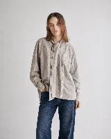 Camisa gris de algodón con textura sutil, corte relajado y mangas amplias. Cuenta con cuello mao con lazo largo para anudar, y detalles de puntilla blanca a contratono en la parte delantera y en los puños.