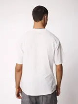Remera blanca de manga corta y cuello redondo con calce holgado, con una pequeña etiqueta oscura en el borde inferior derecho.