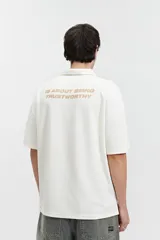 Remera polo color crema con logo bordado en el pecho, de corte amplio y mangas cortas.