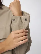 Campera corta de algodón en color beige, con cuello camisero en contraste color marrón, cierre frontal con botones a presión y dos bolsillos frontales tipo cargo.