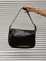 Bolso de hombro con diseño animal print de leopardo, confeccionado en cuero. Presenta una correa ajustable con hebilla metálica y detalles de ojales decorativos en los laterales.