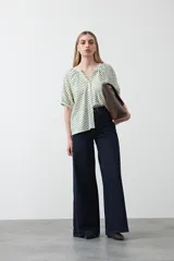 Camisa de viscosa con estampado de lunares pequeños en negro sobre fondo blanco o crema. Presenta escote en V con abertura y botones frontales, y mangas cortas abullonadas.