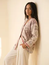 Cardigan de punto color crema con diseño de bordados geométricos en tonos tierra y ribete con patrón de cuadros rojos en los bordes. Presenta un corte recto, cuello en V y mangas largas.