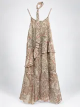 Conjunto compuesto por un vestido largo sin mangas de estampado paisley con volados en capas y un pañuelito a tono, acompañado por una chaqueta beige de manga corta con solapas, botón frontal y bolsillos.