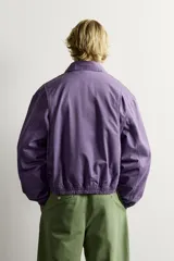 Cazadora regular fit de algodón color violeta con efecto lavado, cuello solapa y cierre de cremallera de doble dirección. Posee bordado frontal de gráficos Fruit of the Loom, bolsillos de vivo en la cadera y acabados con elástico.
