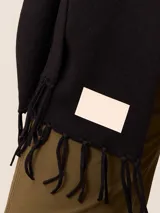 Pashmina de textura suave y color crema, con diseño liso y terminaciones en flecos en los extremos. Incluye una etiqueta decorativa en una de las esquinas.