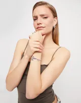 Pulsera elástica con cuentas plateadas y cristales azules. Presenta un dije con forma de libélula y otro con la palabra "Suerte".