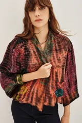 Kimono de estilo abierto con mangas anchas, confeccionado en viscosa con un diseño estampado que combina patrones tipo tie-dye y patchwork en tonos vibrantes. Presenta detalles de aplicaciones decorativas y forro interior.