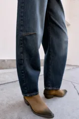 Jeans de tiro medio, color azul oscuro lavado, con corte balloon fit (holgado en muslos y estrechado en el tobillo). Presenta cinco bolsillos, cierre frontal con botones y detalle de trabilla con hebilla en la parte trasera de la cintura.