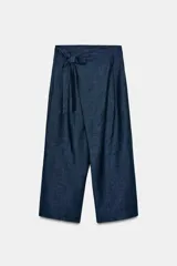 Pantalón azul de tiro medio con corte ancho, cierre frontal cruzado tipo pareo con botón interior y lazada.