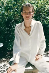 Camisa color tostado de manga larga con pliegues, cuello de solapa y cierre frontal con botones forrados. Presenta diseño de bajo asimétrico.