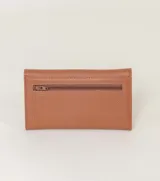 Billetera tipo sobre color champagne, con textura de cuero granulado y cierre de solapa. Presenta una placa metálica rectangular con el nombre de la marca grabado en el frente.
