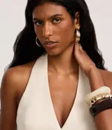 Chaleco color crudo confeccionado en viscolino, con escote halter, cierre frontal con botones, bolsillos delanteros falsos y bajo en V.