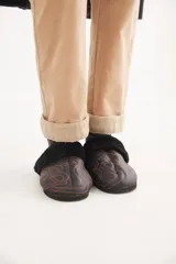 Pantalón de corte recto y tiro medio, confeccionado en pana fina con lycra. Presenta pinzas frontales, bolsillos laterales y traseros, y un botón en tono oro. El diseño destaca por su ruedo con detalle de paño espigado visible al doblarlo y un pin bordado de la marca en el bolsillo delantero.