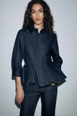 Camisa de denim azul oscuro con cuello solapa, manga larga con puños y diseño entallado con bajo estilo peplum. Cierre frontal con botones ocultos bajo solapa.