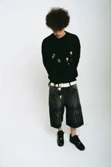 Bermuda de jean color negro con lavado acid wash gris. Presenta un corte baggy y detalles bordados en plateado y blanco que simulan ondas o llamas en la parte frontal superior e inferior.