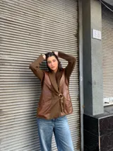 Chaqueta de punto color marrón con cuello de punto acanalado y solapas de cuero. Presenta un cinturón de tela con hebilla dorada y bolsillos de cuero con detalles de cordones.