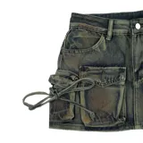 Minifalda de jean con efecto batik en tonos verde y marrón, de corte ajustado. Presenta un diseño tipo cargo con dos bolsillos pequeños superiores y dos bolsillos grandes laterales con solapa.