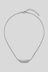 Collar de metal plateado con cadena fina estilo serpiente y un dije tubular liso y curvado en el centro. Cuenta con cierre de mosquetón y cadena de alargue.