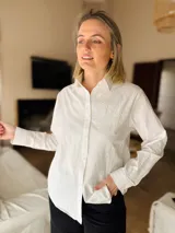 Camisa de manga larga confeccionada en popelina natural, con cuello clásico y cierre frontal de botones. Presenta un delicado bordado floral a tono sobre el hombro izquierdo.