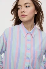 Camisa oversize de manga larga con estampado de rayas verticales en tonos rosado, celeste y verde menta. Cuenta con cuello camisero, cierre frontal con botones y un bolsillo aplicado en el pecho.