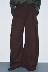 Pantalón ancho de tiro medio color marrón oscuro, confeccionado en tejido con lana. Presenta pinzas delanteras, cinturón ajustable con hebilla metálica y bolsillos cargo de plastrón en las piernas.
