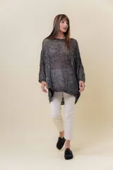 Buzo de tejido liviano y calado con brillo sutil, color gris oscuro o negro. Presenta un calce amplio y mangas amplias, con un detalle de tiras entrelazadas en la espalda. El largo es irregular, más largo en la parte trasera.