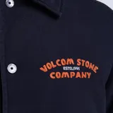 Campera tipo coach negra con cierre frontal de botones metálicos, cuello clásico y puños elásticos. Presenta un estampado bordado en color naranja en el pecho con la inscripción Volcom Stone Company.