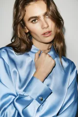 Camisa de cuello solapa y manga larga, confeccionada en tejido satinado con acabado brillante. Presenta cierre frontal con botones y bajo asimétrico.