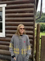 Saco de punto gris con diseño geométrico en color amarillo, cierre frontal con botones, cuello redondo y bordado de corazón pequeño en el pecho.