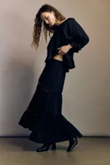 Pollera larga de color negro con elegantes alforzas e inserciones de encaje. Modelo de corte holgado con cintura elástica en la parte posterior.