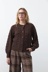Cardigan de tejido de punto color marrón chocolate, con diseño de trenzas en el frente y mangas. Presenta cuello redondo, cierre frontal con botones al tono y puños acanalados.