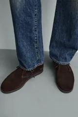 Bota de cordones tipo derby, color marrón oscuro, fabricada en piel con acabado serraje. Tiene plantilla interior de piel, horma redonda y suela fina a contraste.