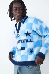 Sweater de tejido de punto con diseño a cuadros en tonos celestes y azules. Presenta cuello en V con solapa, mangas largas y detalles estampados al frente con estrellas y texto deportivo.